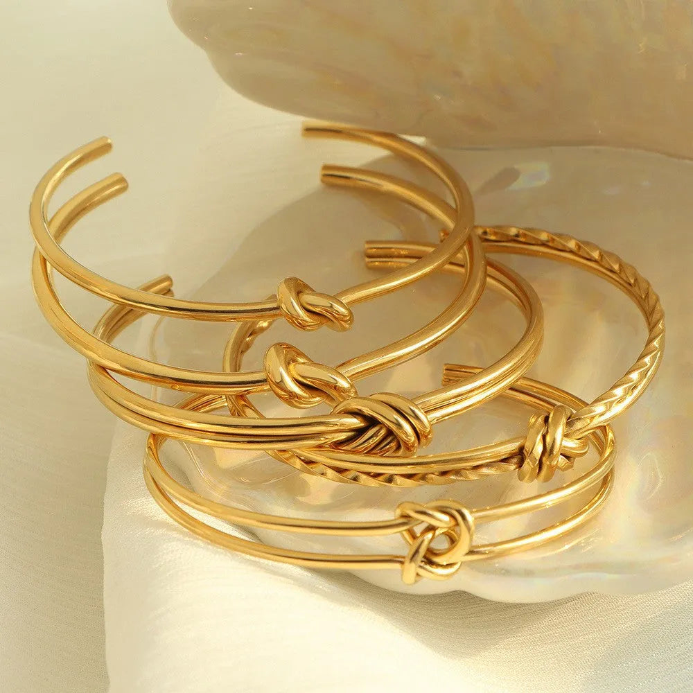 Open C-shaped stainless steel bracelet with knotted double layer design in gold or silver finish.