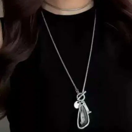 Long geometric alloy pendant necklace with snake bones chain on a plaid background.