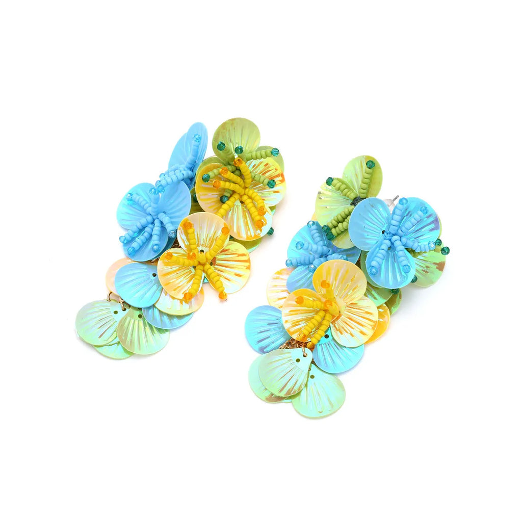 Handmade exaggerated floral earrings with colourful string beads and leaves on a purple background.