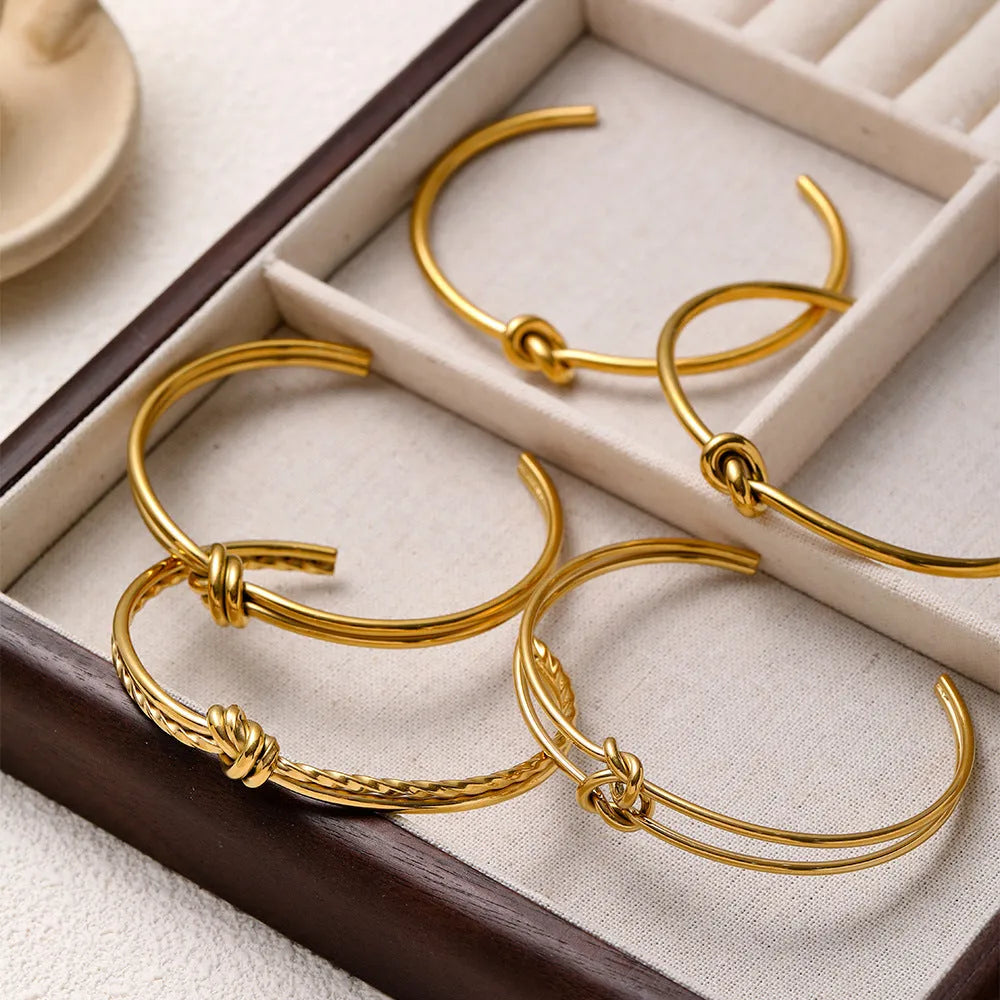 Open C-shaped stainless steel bracelet with knotted double layer design in gold or silver finish.