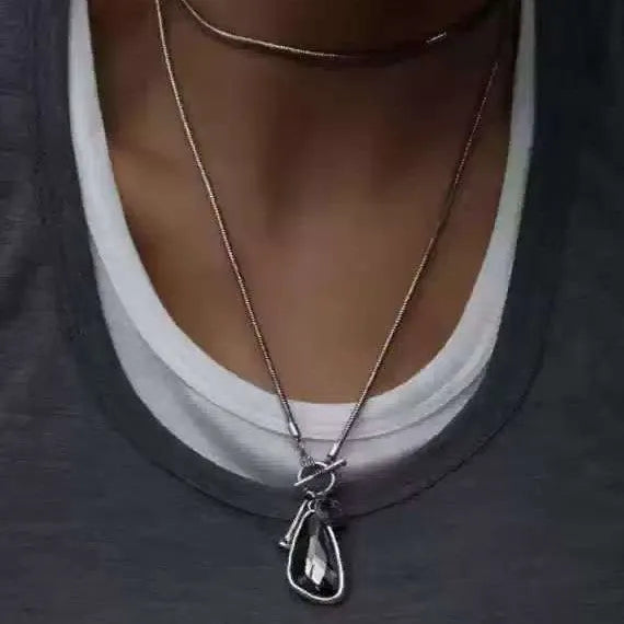 Long geometric alloy pendant necklace with snake bones chain on a plaid background.
