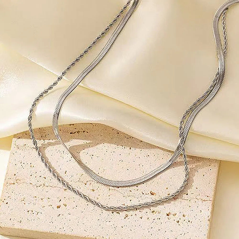 Close-up of a geometric double-layer twist pendant necklace on a textured snake bones chain.