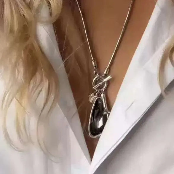Long geometric alloy pendant necklace with snake bones chain on a plaid background.