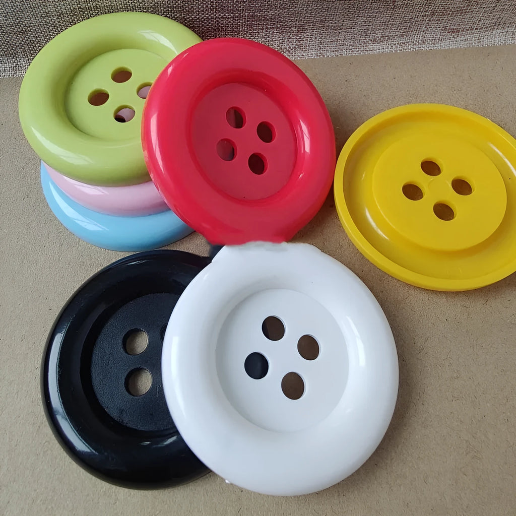 Plastic nylon oversized round button with four holes in various colours and sizes on a white background.
