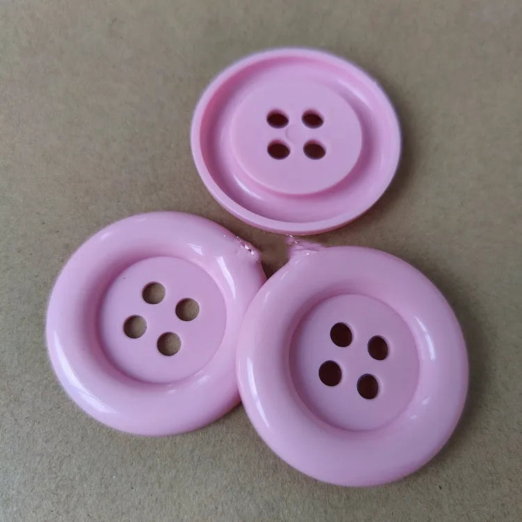 Plastic nylon oversized round button with four holes in various colours and sizes on a white background.