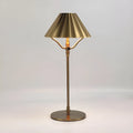 Gold-coloured alloy desk lamp with a cylindrical shade on a wooden desk.