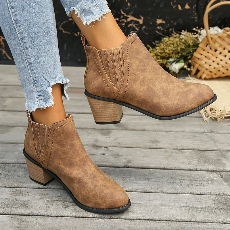 Black pointed toe ankle boots with a thick square low heel on a woman's foot.