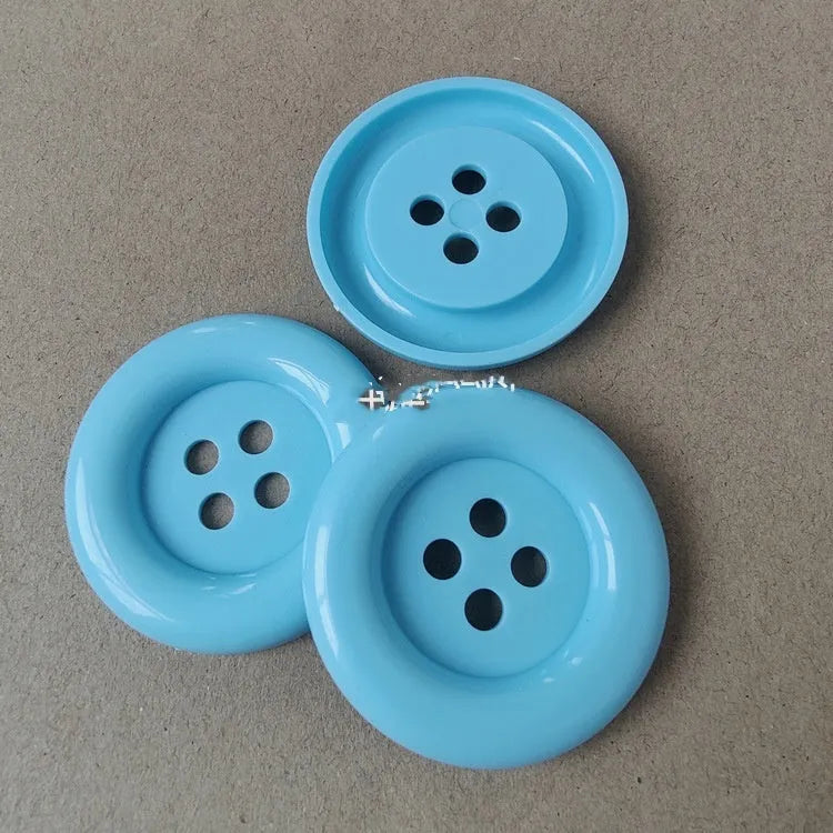 Plastic nylon oversized round button with four holes in various colours and sizes on a white background.