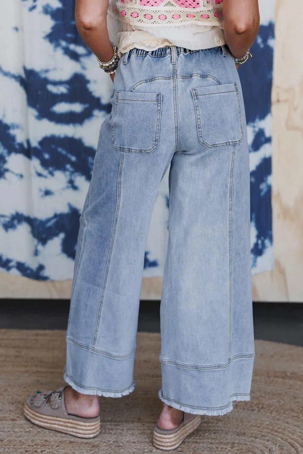 Beau blue wide leg denim trousers with a drawstring waist and raw hem on a hanger