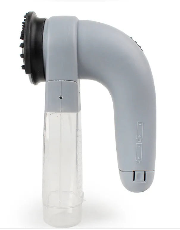 Grey handheld electric pet hair remover brush with soft rubber head, shown removing fur from upholstery.