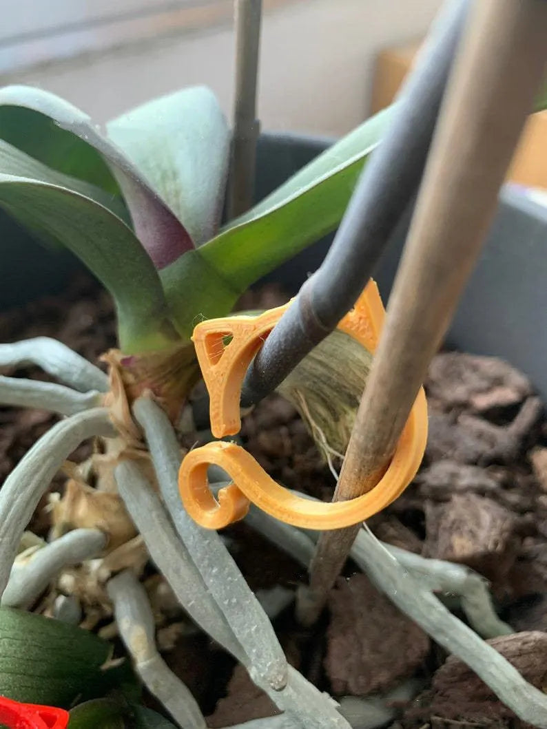 Small red cat-shaped plastic clip for plant support on a green leaf.