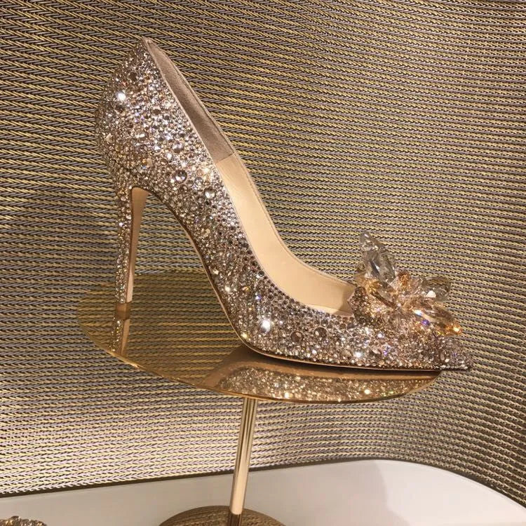 Gold women's pointed toe stiletto heels with rhinestone and bow decoration on a sequin cloth upper.