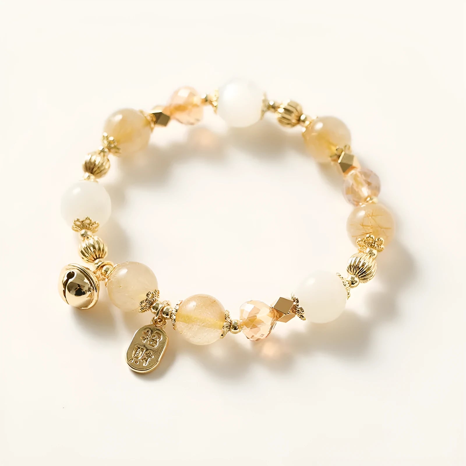 Gold rutilated quartz bracelet with bell charm on wrist