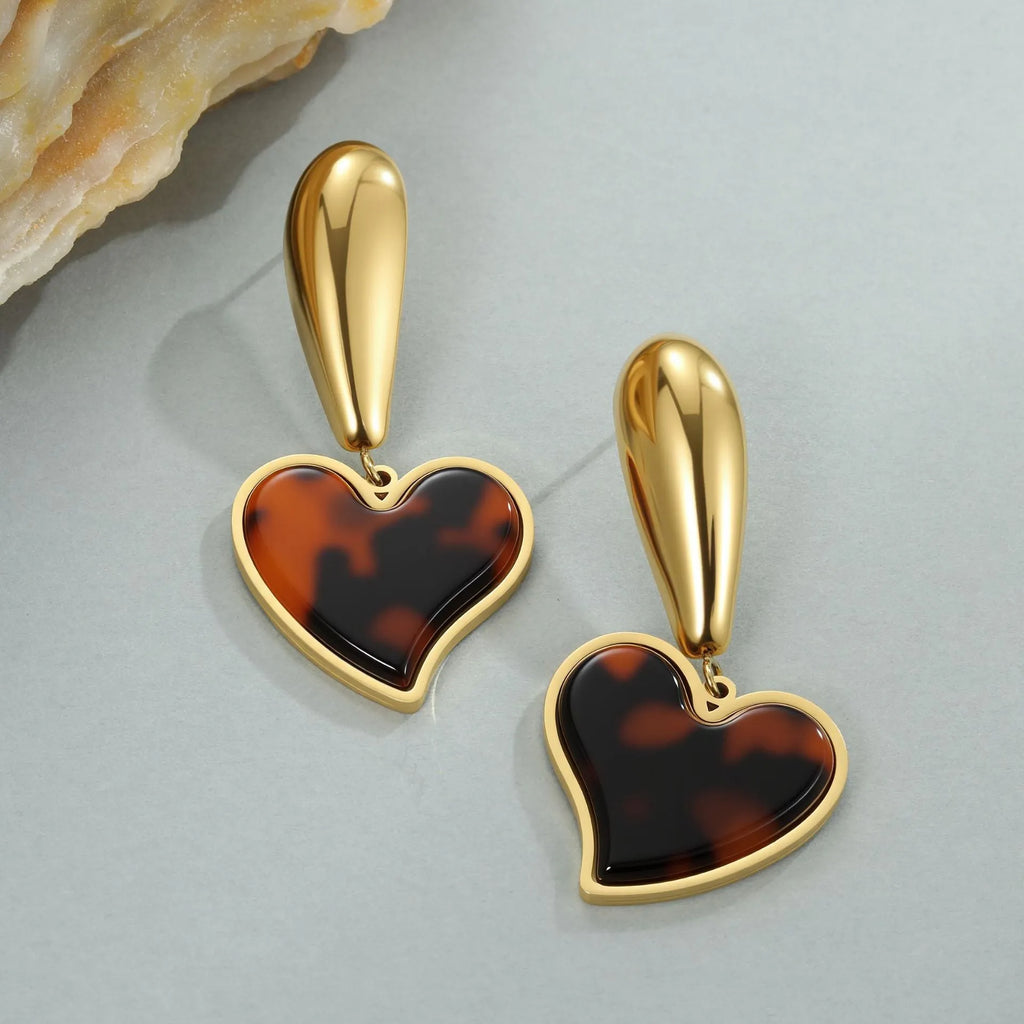 A pair of gold-coloured geometric earrings with a heart shape and a floral design on a white background.