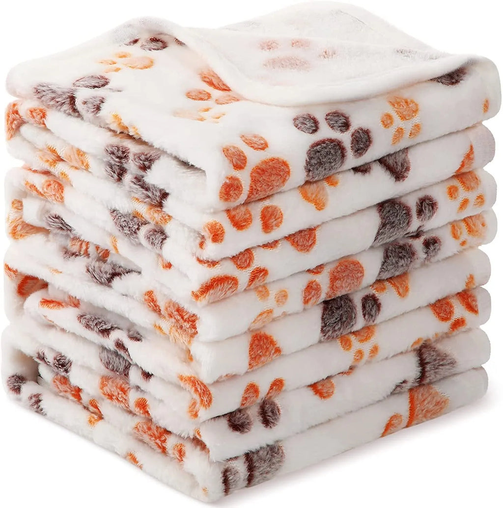 Coral fleece pet blanket with dog's paw print pattern in beige, shown in a large size on a dog bed.