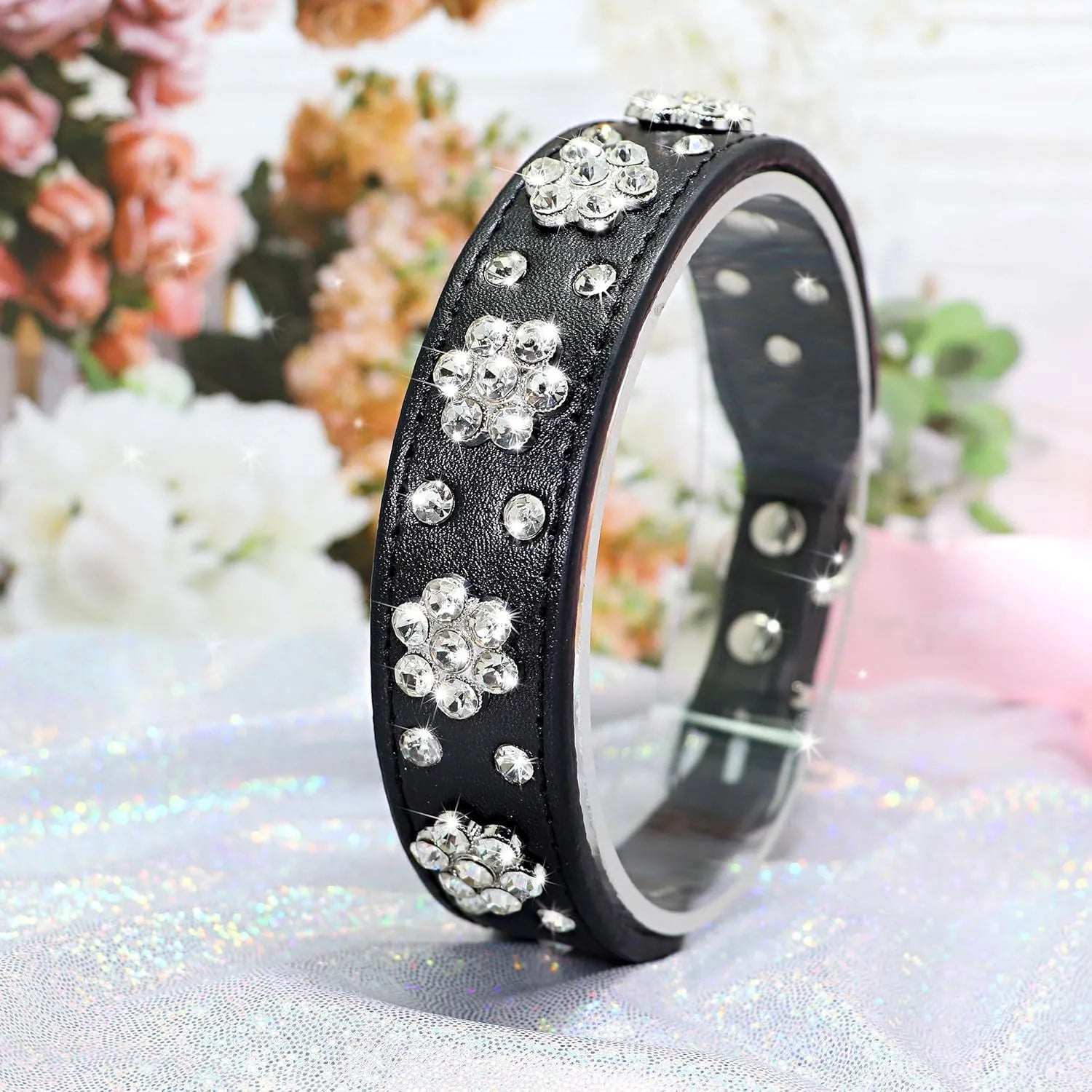 Close-up of a black PU leather dog collar with sparkling rhinestone flowers and a metal D-ring.