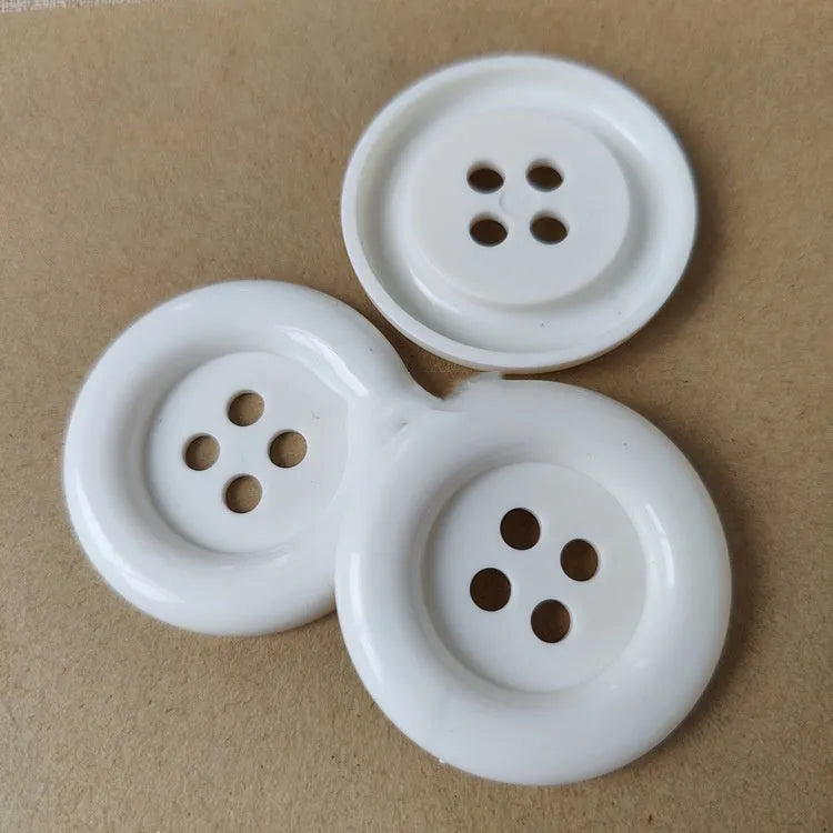 Plastic nylon oversized round button with four holes in various colours and sizes on a white background.