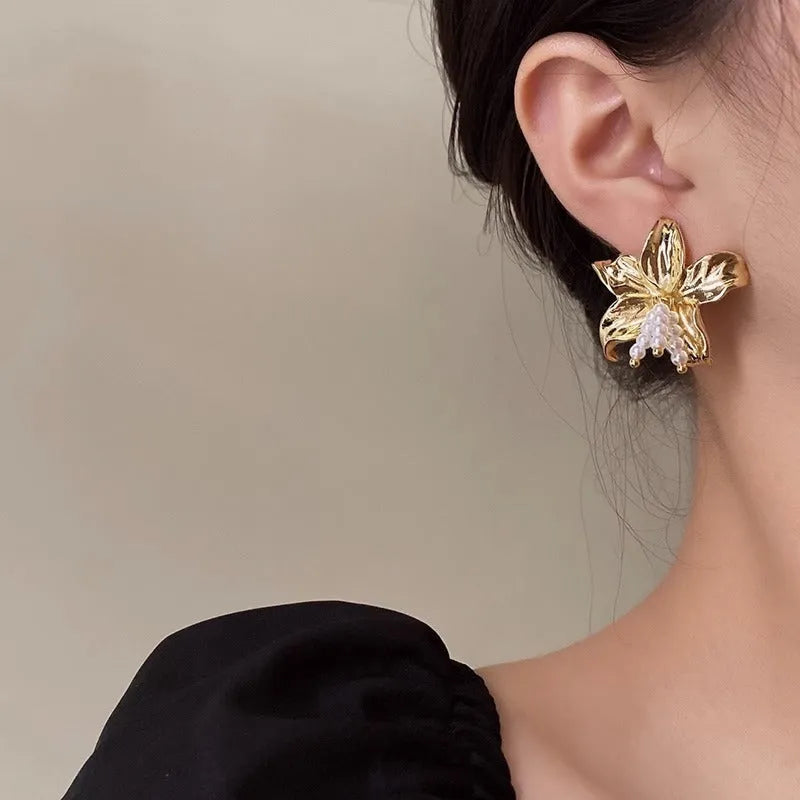 A pair of exaggerated gold metal flower earrings with pearl centres, showing a niche floral jewellery design.