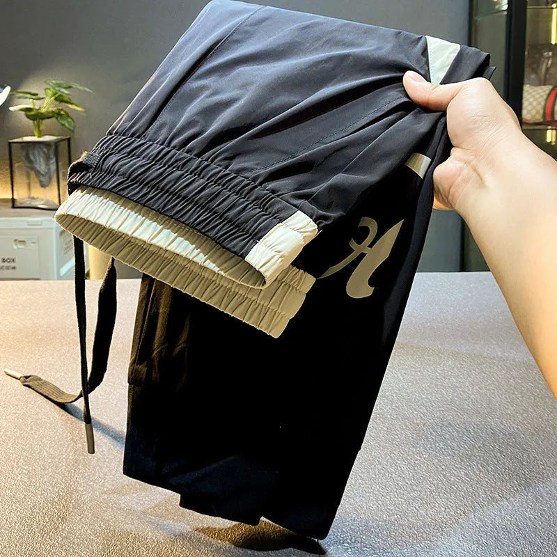 Black men's cropped casual trousers with an ankle-band cuff, laid flat to show the slim fit and cotton blend fabric.