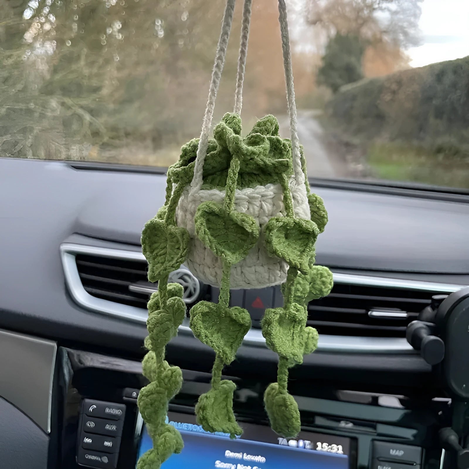 Green and white knitted wool car plant decoration with hanging rope on a car dashboard