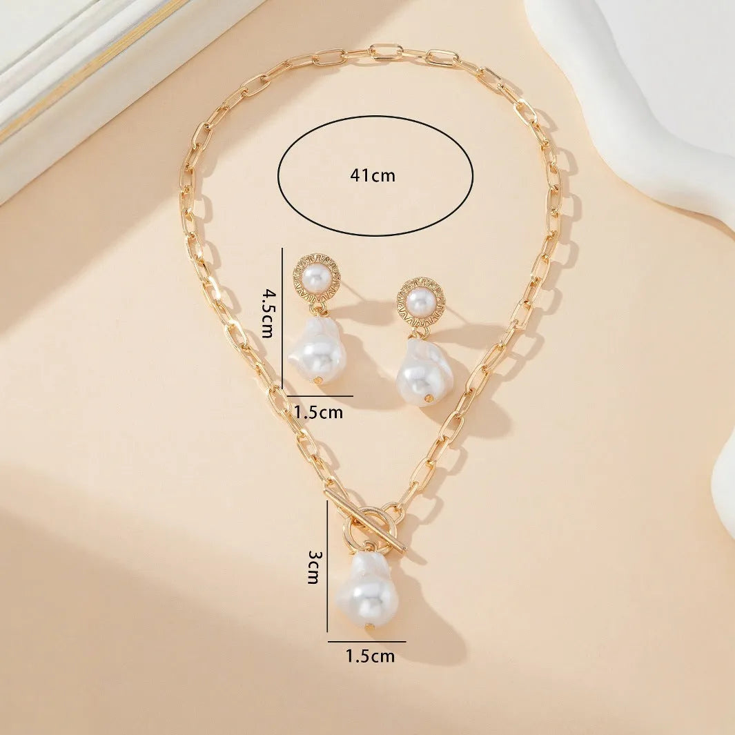 Gold-coloured retro baroque pearl pendant necklace and matching stud earrings set on a dark background.
