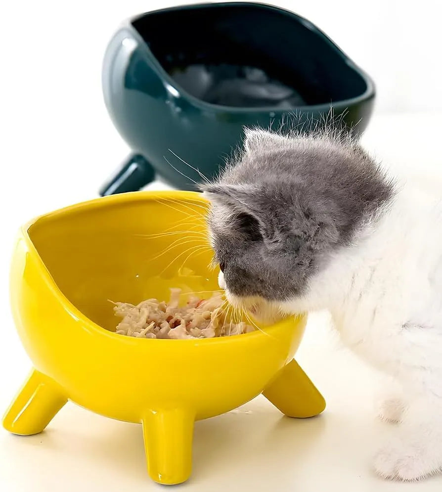 Green ceramic cat food bowl with four legs and rounded arc design on wooden floor