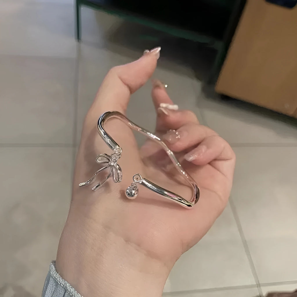 Silver adjustable bracelet with a bow charm and a visible bell-opening clasp on a white background.