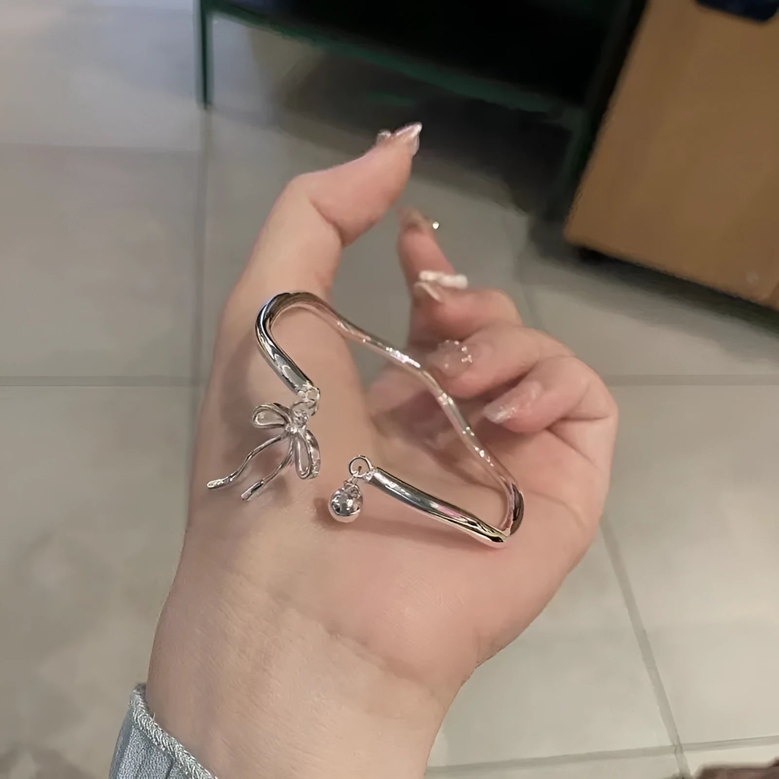 Silver adjustable bracelet with a bow charm and a visible bell-opening clasp on a white background.