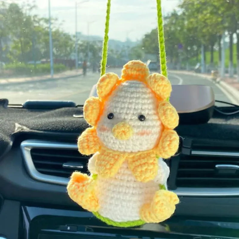 Green and white knitted wool car plant decoration with hanging rope on a car dashboard