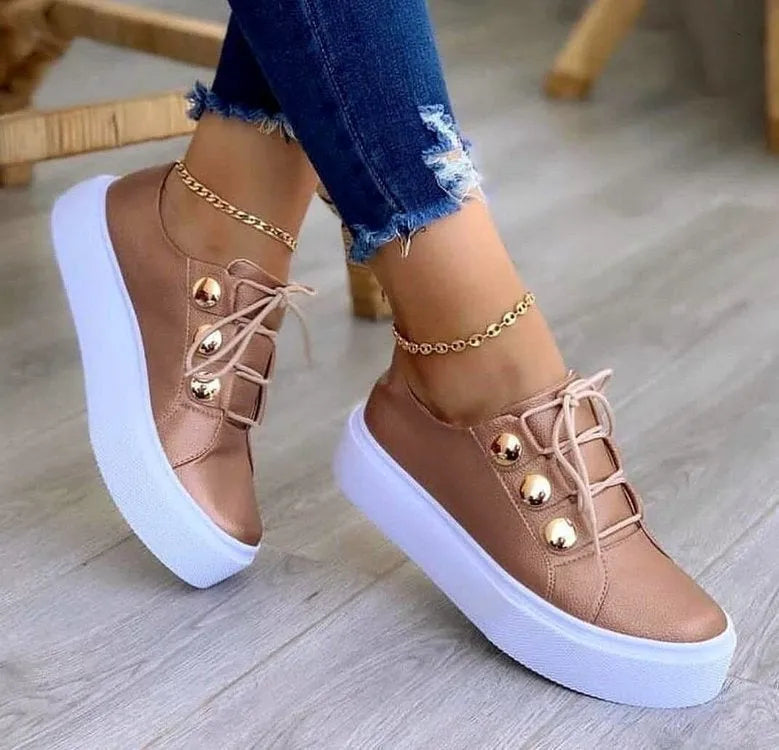 Women's white lace-up flat sneakers with silver rivet detailing on a round toe.