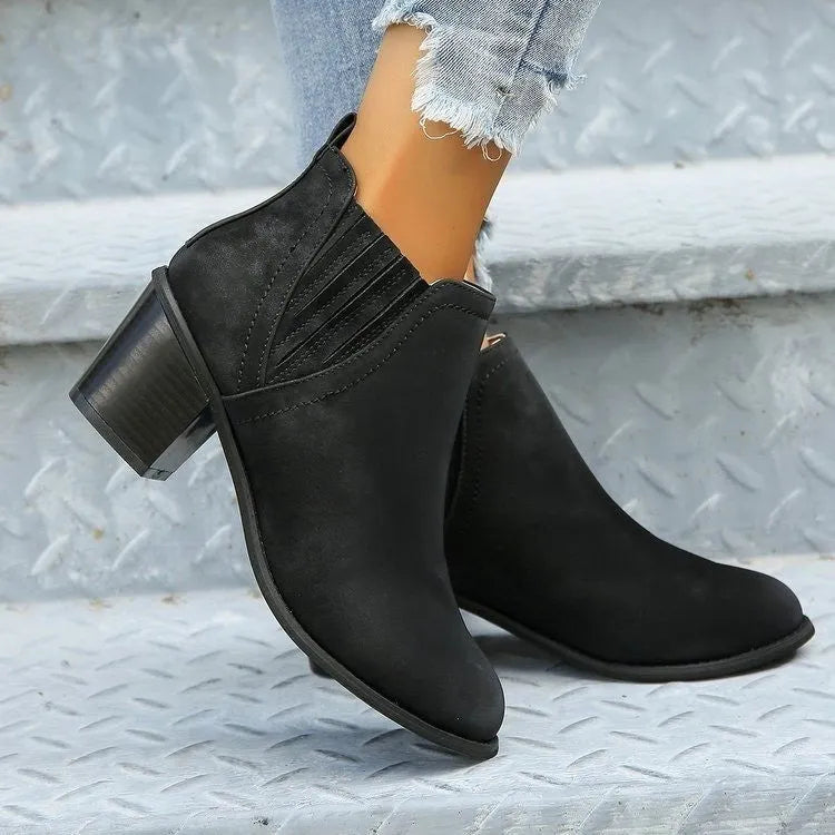 Black pointed toe ankle boots with a thick square low heel on a woman's foot.