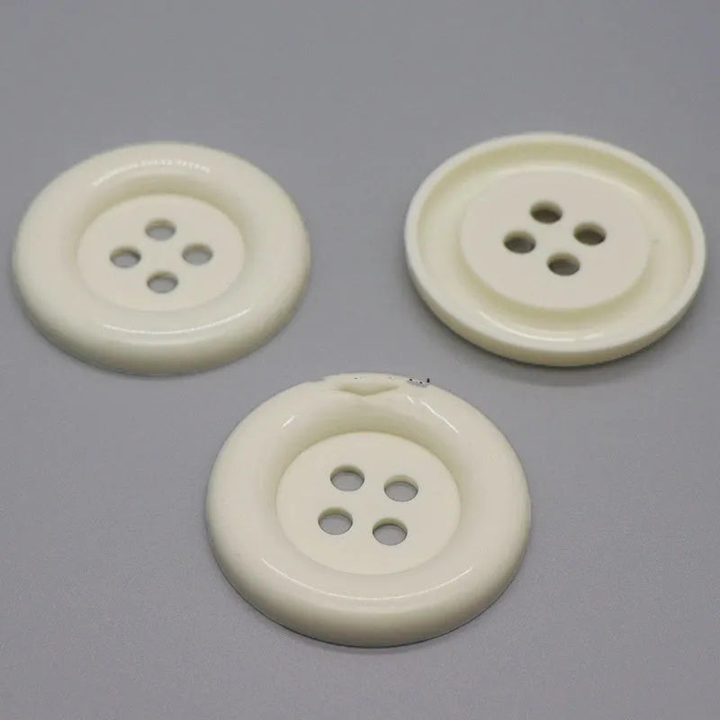 Plastic nylon oversized round button with four holes in various colours and sizes on a white background.