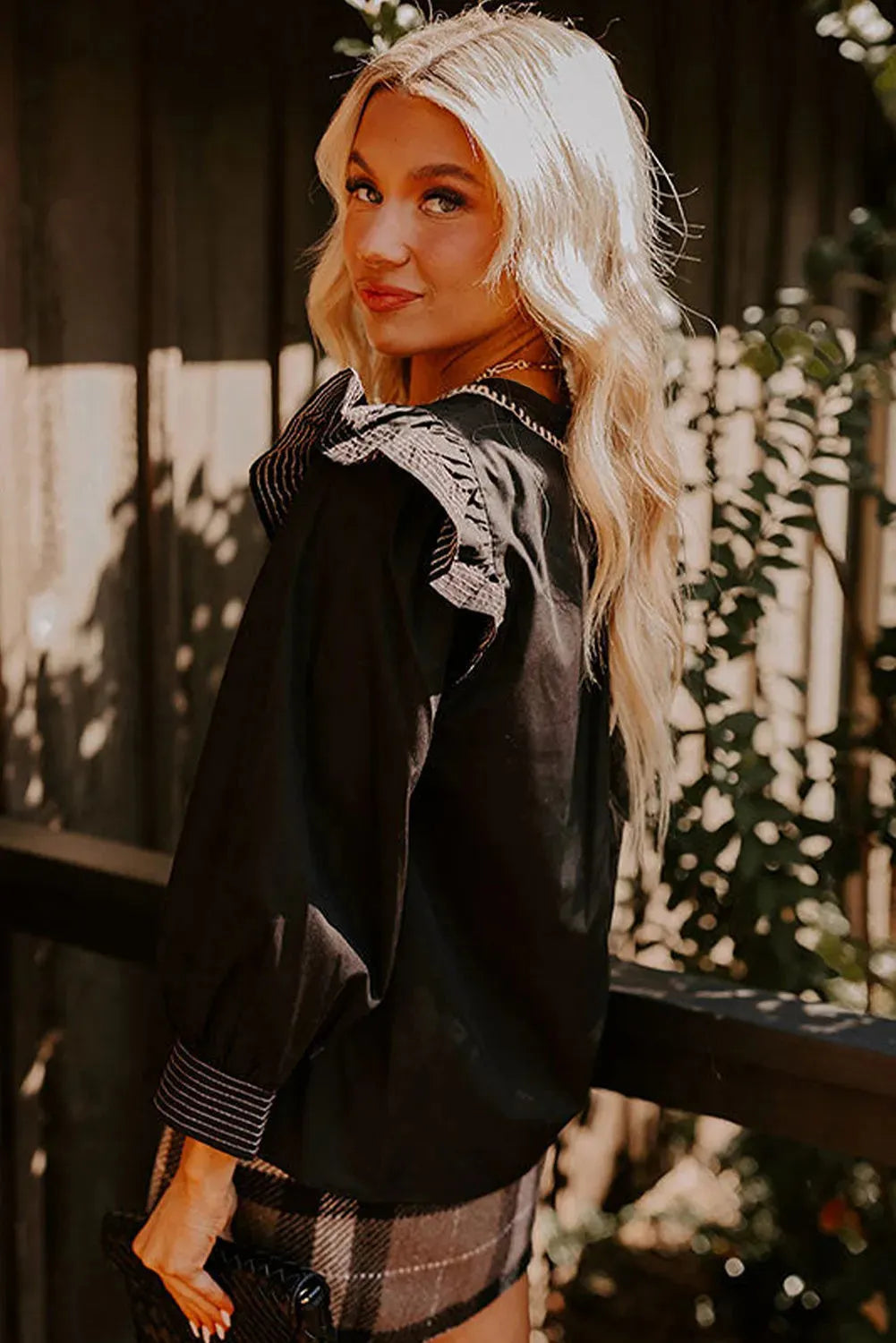 Black women's blouse with V-neck, long ruffle sleeves, and contrast stitch detail.