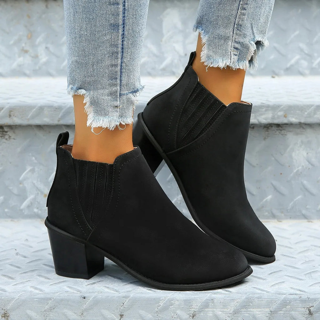 Black pointed toe ankle boots with a thick square low heel on a woman's foot.