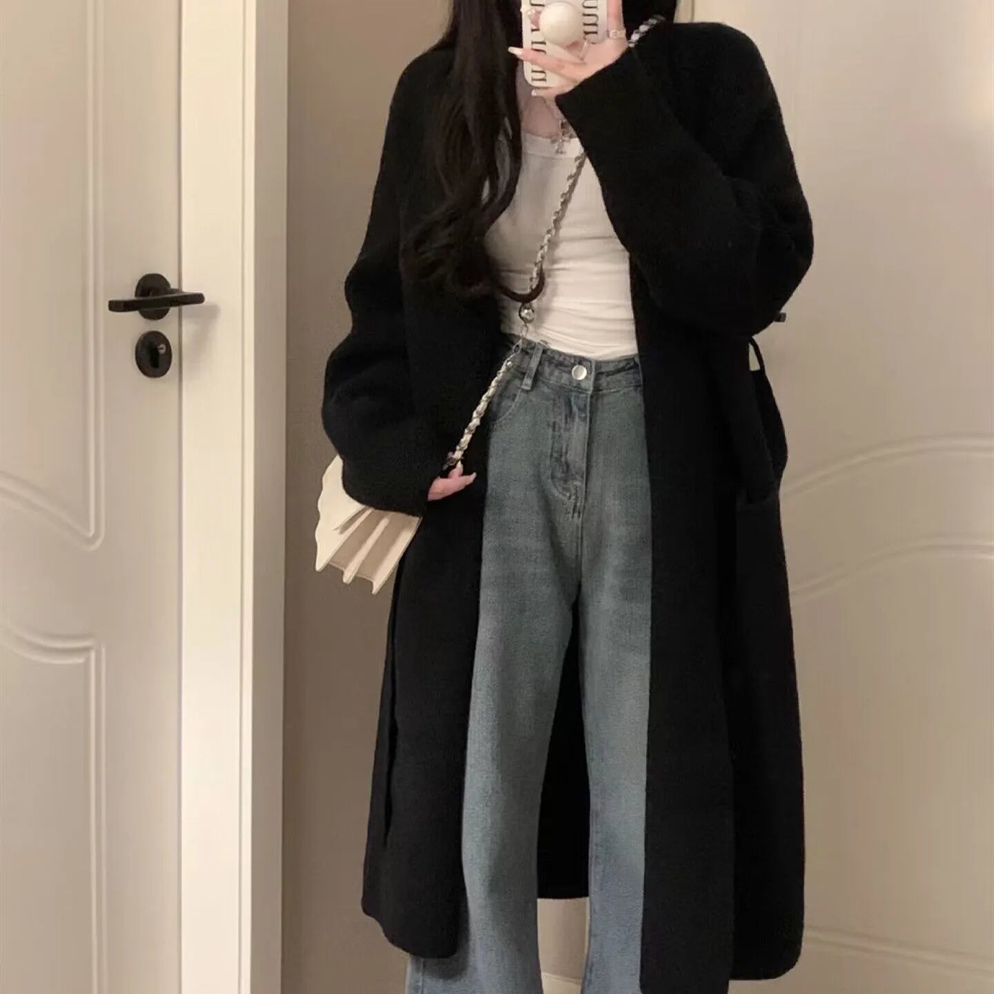 Loose black knitted women's cardigan with a 3D pattern, shown open over a white top.