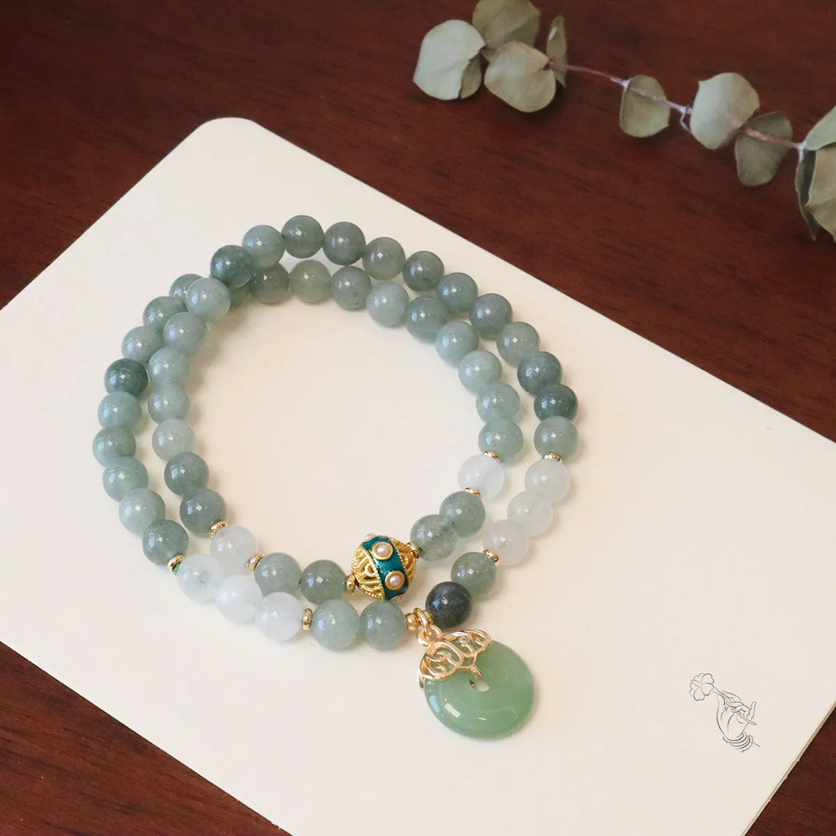 Close-up of a women's Myanmar jade bracelet with a silver geometric safety buckle pendant and lucky bead charms.