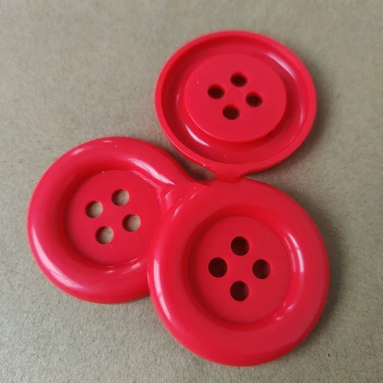 Plastic nylon oversized round button with four holes in various colours and sizes on a white background.