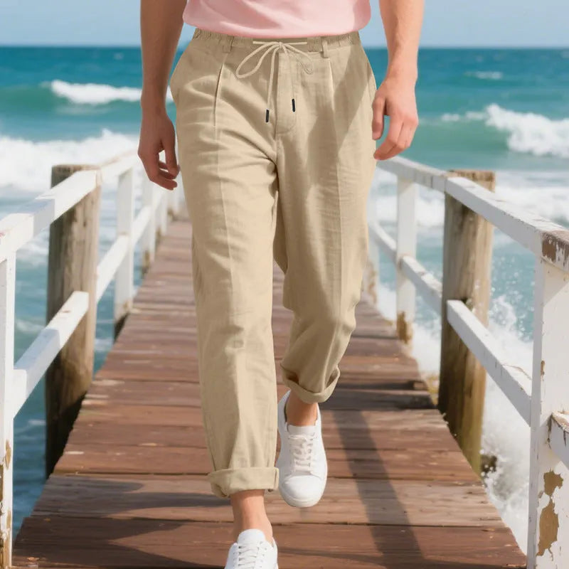 Men's straight leg linen trousers in light khaki colour with drawstring waist, laid flat.