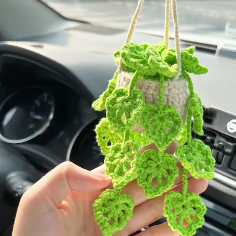 Green and white knitted wool car plant decoration with hanging rope on a car dashboard