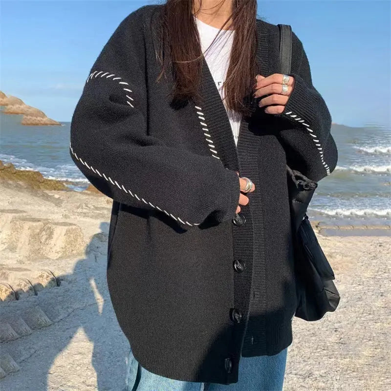 Women's loose fit black knitted cardigan top coat with long sleeves, hanging on a hanger.