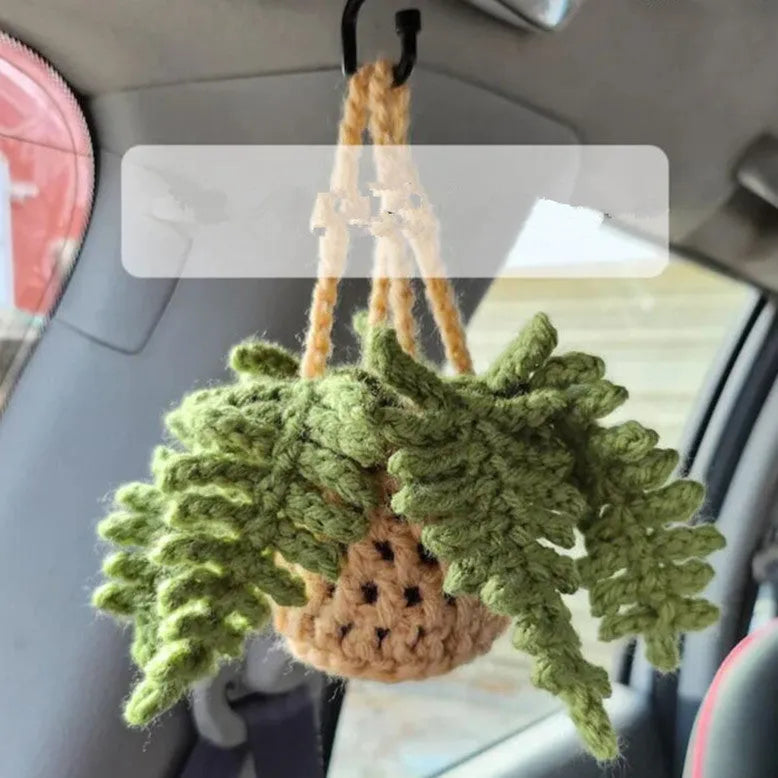 Green and white knitted wool car plant decoration with hanging rope on a car dashboard