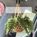 Green and white knitted wool car plant decoration with hanging rope on a car dashboard