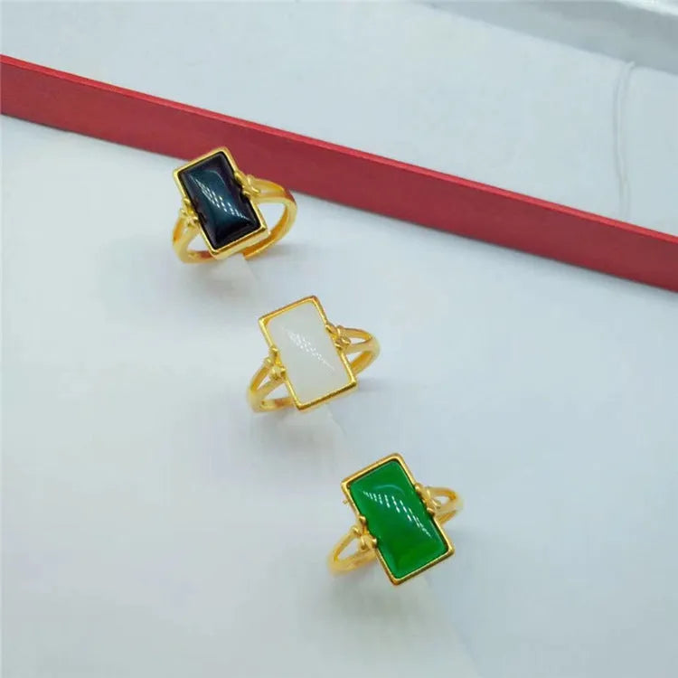 Adjustable brass gold-plated ring with a central green gemstone on a model's hand.