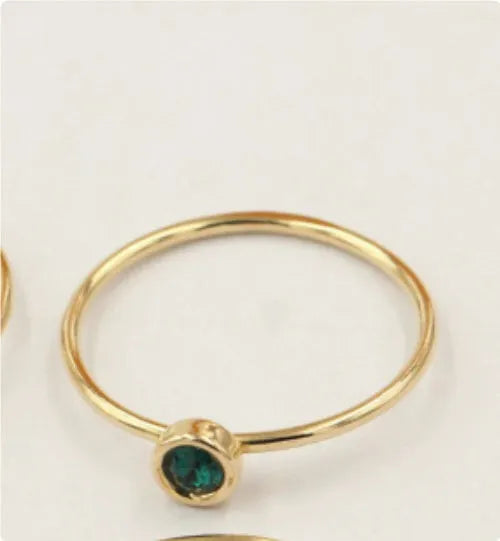 Women's 14K gilded gold-filled zircon copper knuckle ring in green, blue, dark red, or white on a finger.