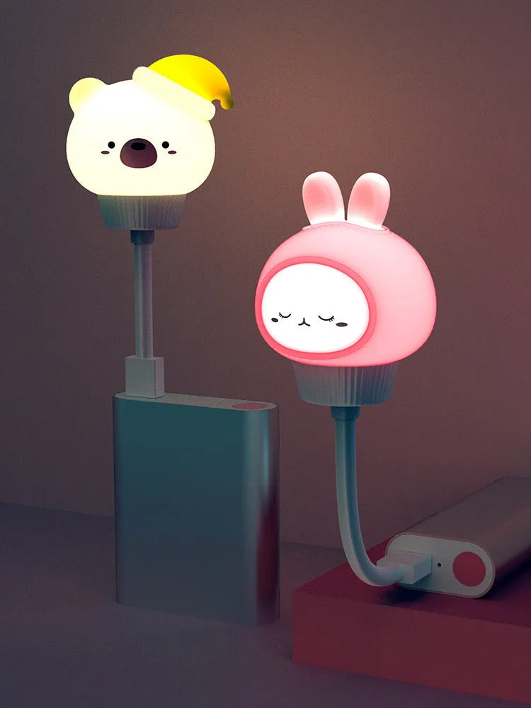 Small cartoon bear-shaped USB night light with remote control on a bedside table.