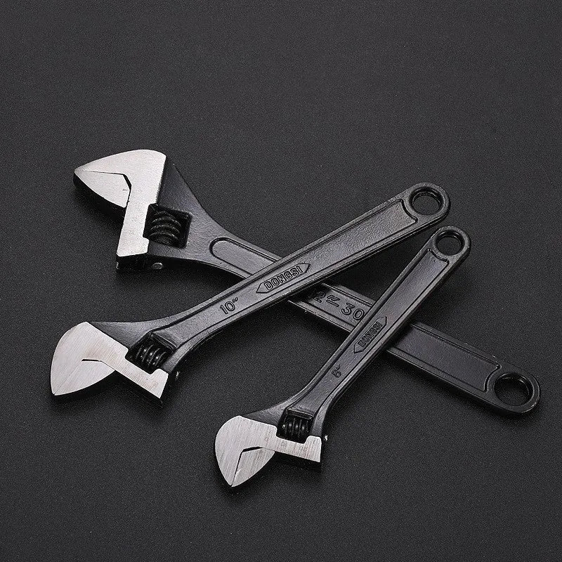 Black stainless steel adjustable open-end wrench on a workbench, showing size markings and ergonomic handle.