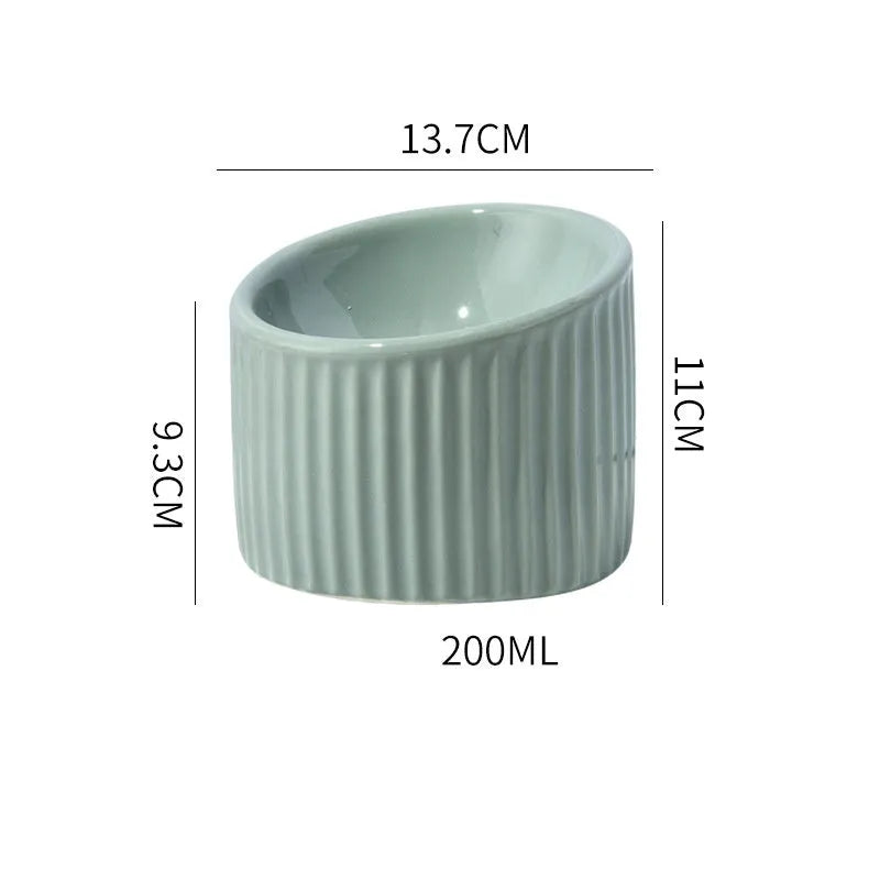 Dark green ceramic elevated cat bowl with tilted, round whisker-friendly design on a wooden floor.