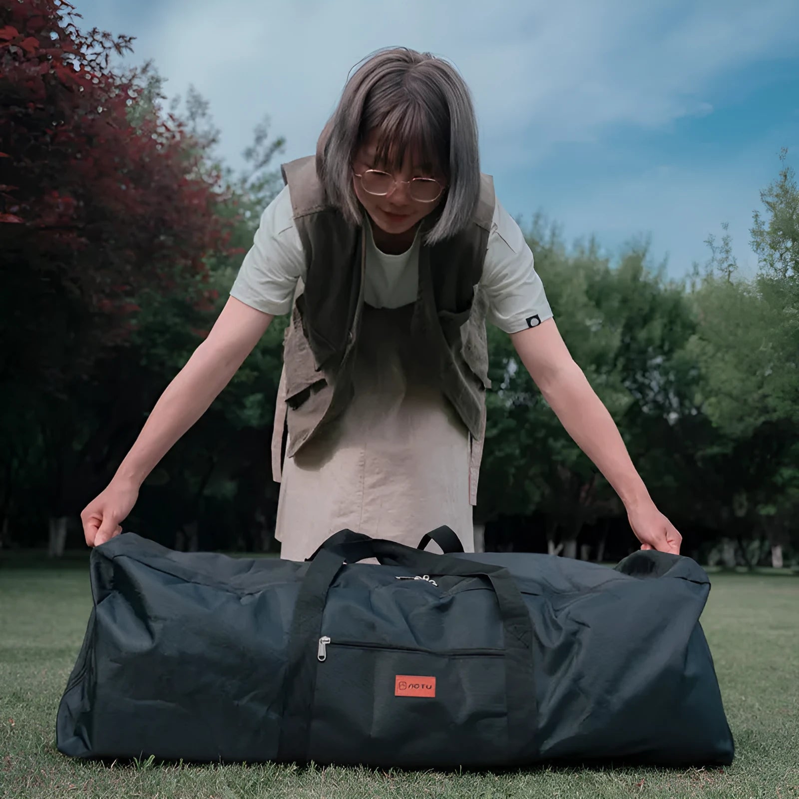 Green waterproof camping storage bag with carry handles, shown carrying a folding table and chairs.