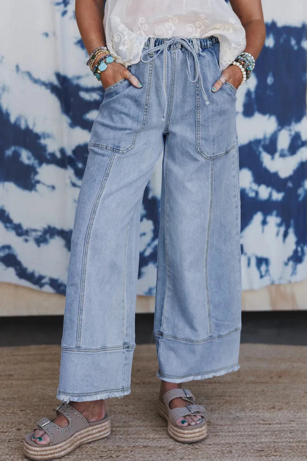 Beau blue wide leg denim trousers with a drawstring waist and raw hem on a hanger