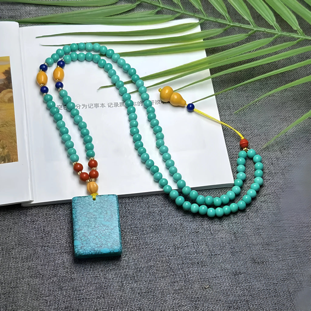 Turquoise stone pendant with hand-woven mesh flower design on a ball bead necklace chain.